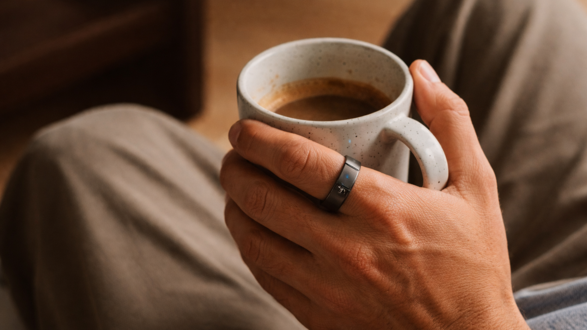 A hand of a man wearing an ultrahuman ring holding a coffee mug.